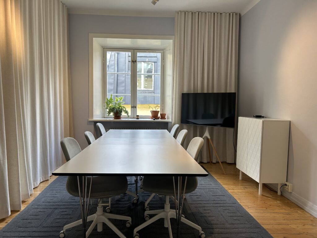 Ett mindre kontorsrum med en TV framför ett bord med sex stolar. 
